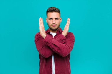 Genç, İspanyol bir adam senin tavırlarından rahatsız ve bıkkın görünüyor. Yeter artık! Eller önde, mavi arka planda durmanı söylüyor.