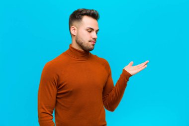 Genç İspanyol bir adam mutlu ve gülümsüyor. Mavi arka planda duran bir nesneye ya da konsepte bakıyor.