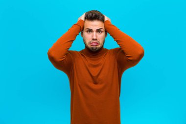 Genç İspanyol adam hayal kırıklığına uğramış ve sıkılmış hissediyor, başarısızlıktan bıkmış ve bıkmış, mavi arka plana karşı sıkıcı, sıkıcı görevlerden bıkmış