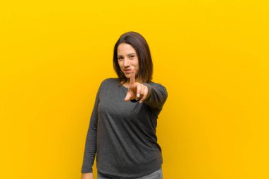 Latin Amerikalı kadın gururla gülümsüyor ve gururla bir numaralı pozu veriyor. Sarı duvara karşı izole edilmiş bir lider gibi hissediyor.