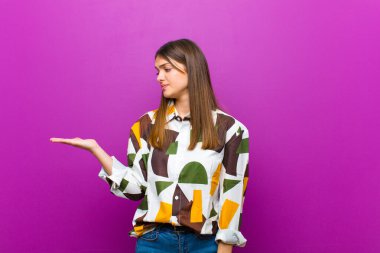 Genç, güzel bir kadın kendini mutlu hissediyor ve gülümsüyor. Mor arka planda duran bir nesneye ya da konsepte bakıyor.