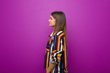 Profil görünümünde genç, güzel bir kadın uzayı kopyalamaya çalışıyor, düşünüyor, hayal ediyor ya da hayal kuruyor mor arka plana karşı.