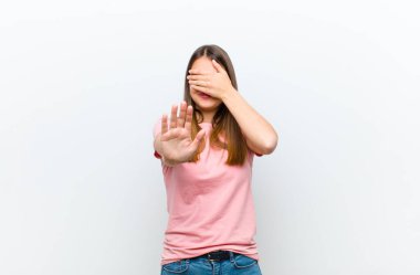 Genç, güzel bir kadın yüzünü eliyle kapatıyor ve kamerayı durdurmak için diğer elini öne koyuyor. Beyaz arka plandaki fotoğraf ve resimleri reddediyor.