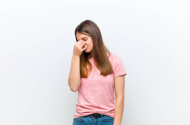 Genç, güzel bir kadın stresli, mutsuz ve hayal kırıklığına uğramış, alnına dokunmuş ve beyaz arka planda şiddetli baş ağrısı çeken.