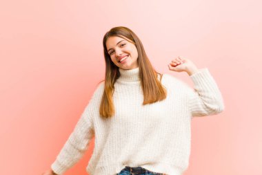 Genç, güzel bir kadın gülümsüyor, kaygısız, rahat ve mutlu hissediyor, dans ediyor ve müzik dinliyor, pembe arka plandaki bir partide eğleniyor.