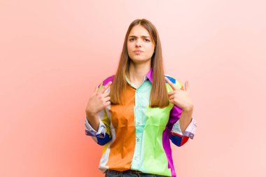 Kötü tavrı olan genç ve güzel bir kadın gururlu ve agresif görünüyor, yukarı bakıyor ya da pembe arka planda ellerle dalga geçiyor.