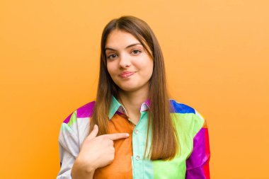 Genç, güzel bir kadın gururlu, kendinden emin ve mutlu görünüyor, gülümsüyor ve kendini işaret ediyor ya da düz arkaplanda bir numaralı işareti izole ediyor.