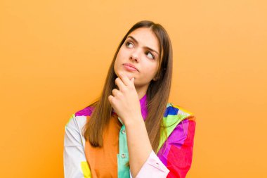 Genç, güzel bir kadın düşünceli, meraklı ya da hayal kuruyor, hayal kuruyor ve düz arkaplana izole edilmiş fotokopi alanını izliyor.