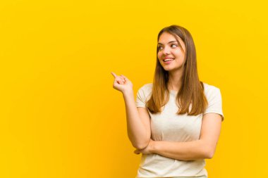 Genç ve güzel bir kadın mutlu bir şekilde gülümsüyor ve yan bakıyor, merak ediyor, düşünüyor ya da turuncu arka plana karşı bir fikri var.