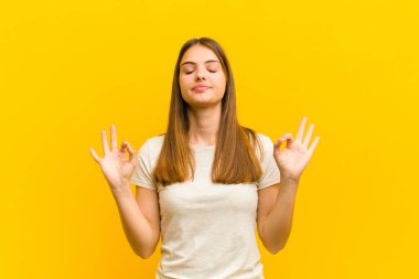 Genç ve güzel bir kadın konsantre olmuş ve meditasyon yapıyor, tatmin olmuş ve rahatlamış hissediyor, düşünüyor ya da turuncu arka plana karşı bir seçim yapıyor.