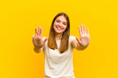 Genç, güzel bir bayan gülümsüyor ve arkadaş canlısı görünüyor. 9 ya da 9 numarayı gösteriyor. Elleri önde, turuncu arka planda geriye doğru sayıyor.