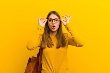 Genç, güzel bir kadın şok olmuş, şaşırmış ve şaşırmış hissediyor. Elinde turuncu arka planda hayrete düşmüş, inanmayan bir bakış var.