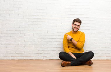 Genç yakışıklı adam tuğla duvar dokusuna karşı evde oturuyor.