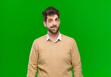 Genç işadamı hangi seçeneği seçeceği konusunda bilgisiz, şaşkın ve kararsız hissediyor, yeşil arka planda sorunu çözmeye çalışıyor