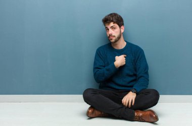 Genç yakışıklı bir adam yerde oturmuş şaşkın, şaşkın ve güvensiz hissediyor. Kendini gösterip kim olduğunu soruyor, ben mi??