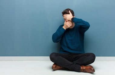 Genç ve yakışıklı bir adam iki eliyle kameraya hayır diyerek yerde oturuyor! Resimler reddediliyor ya da yasaklanıyor