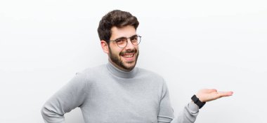 Genç yönetici gülümsüyor, kendinden emin, başarılı ve mutlu hissediyor, beyaz duvara karşı fotokopi alanında fikir veya konsept gösteriyor.