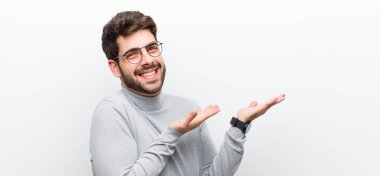 Genç yönetici gururla ve güvenle gülümsüyor, mutlu ve tatmin olmuş hissediyor ve beyaz duvara karşı fotokopi alanında bir konsept gösteriyor.