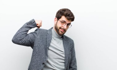 Genç yönetici kendini mutlu, memnun ve güçlü hissediyor, kaslı ve formda, spor salonundan sonra beyaz duvara karşı güçlü görünüyor.