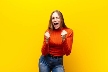 Genç, güzel bir kadın sinirli, sinirli bakışlar ve sıkı yumruklarla bağırıyor. Turuncu arka plana karşı öfkeli hissediyor.