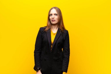 Genç, güzel iş kadını şaşkın ve şaşkın hissediyor, aptal, afallamış bir ifadeyle turuncu arka planda beklenmedik bir şeye bakıyor.