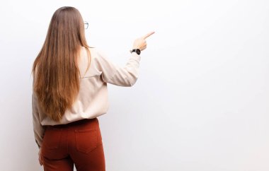 Genç, güzel bir kadın dikilip, fotokopi alanındaki objeyi işaret ediyor, beyaz duvara karşı dikiz manzarası