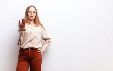 Genç ve güzel bir kadın ciddi, sert, hoşnutsuz ve kızgın görünüyor. Avuç içini açıp beyaz duvara karşı jest yapıyor.