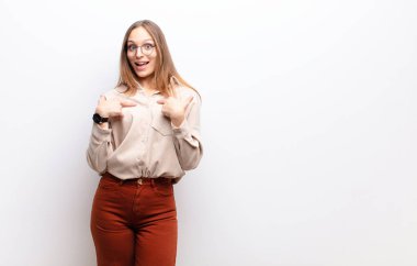 Genç, güzel bir kadın mutlu, şaşırmış ve gururlu hissediyor. Heyecanlı ve şaşkın bir şekilde beyaz duvara bakıyor.