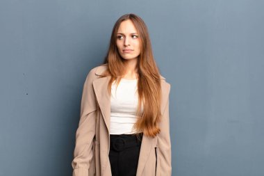 Genç, güzel bir kadın üzgün, üzgün ya da kızgın ve olumsuz bir tavır takınıyor. Gri arka plana karşı anlaşmazlıkla bakıyor.