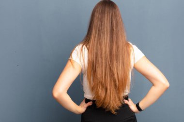 Genç, güzel bir kadın, kafası karışık ya da dolu ya da şüphe ve soru dolu, merak ediyor, elleri kalçasında, arka planı gri