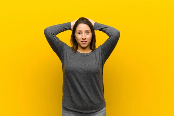latin american woman feeling stressed, worried, anxious or scared, with hands on head, panicking at mistake isolated against yellow wall