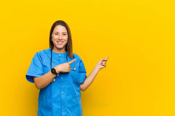 smiling happily and pointing to side and upwards with both hands showing object in copy space isolated against yellow wall