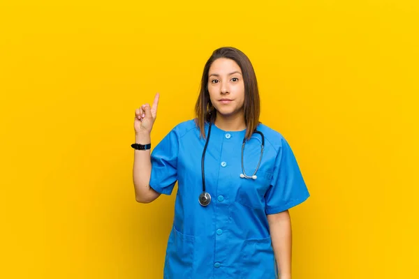 smiling cheerfully and happily, pointing upwards with one hand to copy space isolated against yellow wall