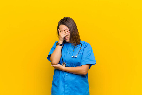 looking stressed, ashamed or upset, with a headache, covering face with hand isolated against yellow wall