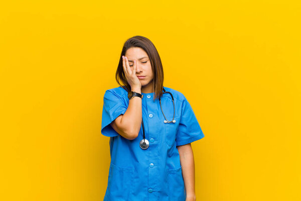 feeling bored, frustrated and sleepy after a tiresome, dull and tedious task, holding face with hand isolated against yellow wall