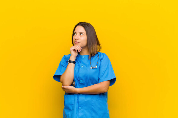 feeling thoughtful, wondering or imagining ideas, daydreaming and looking up to copy space isolated against yellow wall