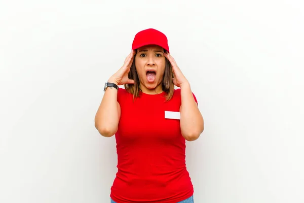 delivery woman raising hands to head, open-mouthed, feeling extremely lucky, surprised, excited and happy against white background