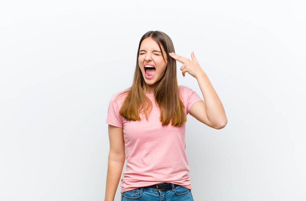young pretty woman looking unhappy and stressed, suicide gesture making gun sign with hand, pointing to head against white background