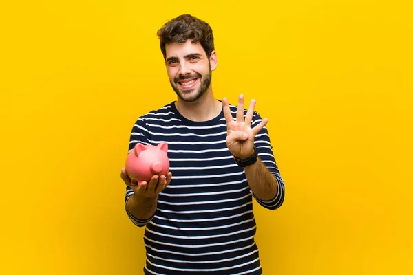 Joven hombre guapo sosteniendo una alcancía contra fondo naranja — Foto de Stock