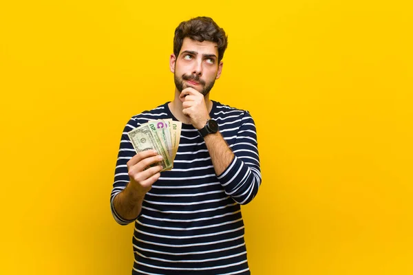 Молодой красивый мужчина с долларовыми банкнотами против оранжевого бэкгру — стоковое фото
