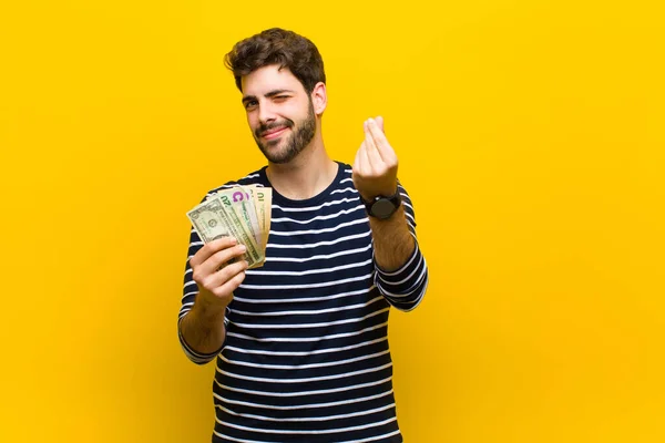 Νεαρός όμορφος άνδρας με χαρτονομίσματα του δολαρίου εναντίον πορτοκαλί backgrou — Φωτογραφία Αρχείου