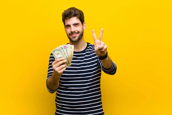 Jonge knappe man met dollarbiljetten tegen oranje backgrou — Stockfoto