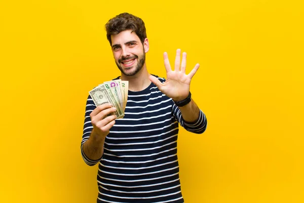 Jonge knappe man met dollarbiljetten tegen oranje backgrou — Stockfoto