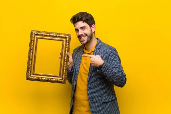 Jovem homem bonito com uma moldura barroca contra backgroun laranja — Fotografia de Stock