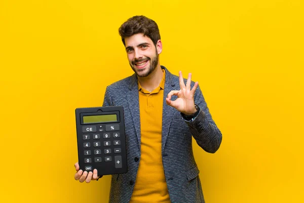 Jovem homem bonito com uma calculadora contra fundo laranja — Fotografia de Stock
