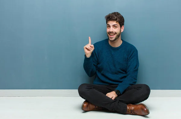 アイデアを実現した後に幸せと興奮の天才のように床に座っている若いハンサムな男 陽気に指を上げる Eureka — ストック写真