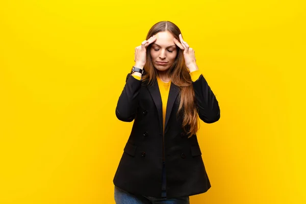 young pretty businesswoman looking stressed and frustrated, working under pressure with a headache and troubled with problems against orange background