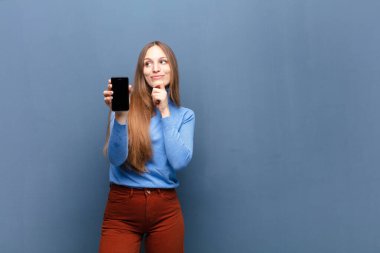 young pretty woman using a smart phone against blue wall with a copy space