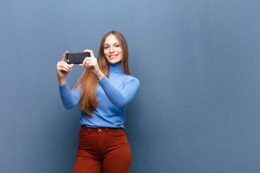young pretty woman using a smart phone against blue wall with a copy space