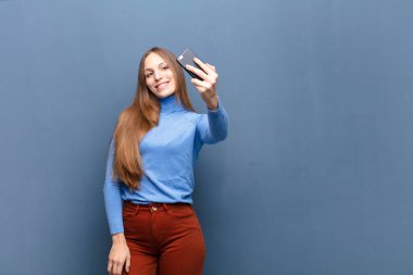 young pretty woman using a smart phone against blue wall with a copy space